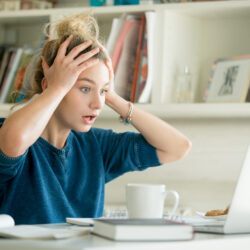 Portrait of an attractive woman at the table with cup and laptop, book, notebook on it, grabbing her head. Bookshelf at the background, concept photo
